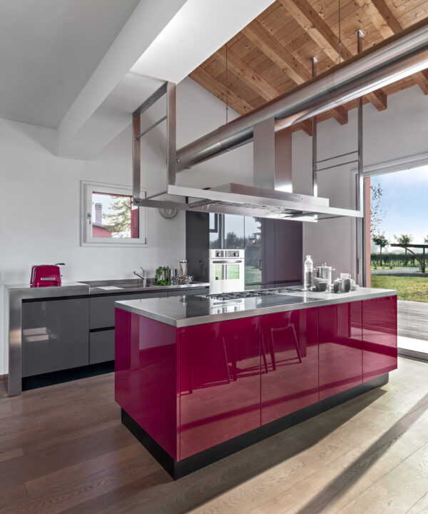 interiors of a modern red lacquered kitchen in the foreground the island kitchen, the floor is in wood and the ceiling is in exposed wooden beams