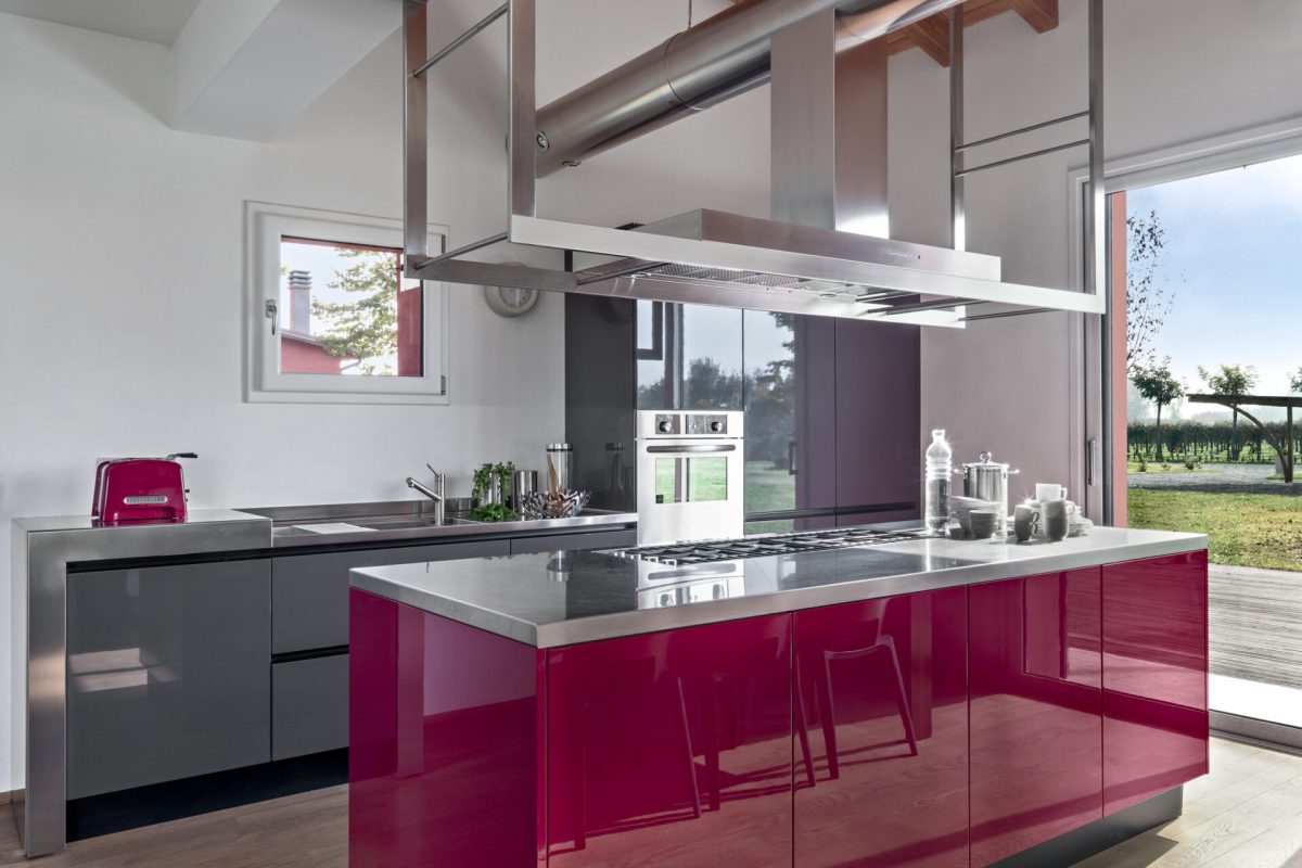 interiors of a modern red lacquered kitchen in the foreground the island kitchen, the floor is in wood and the ceiling is in exposed wooden beams